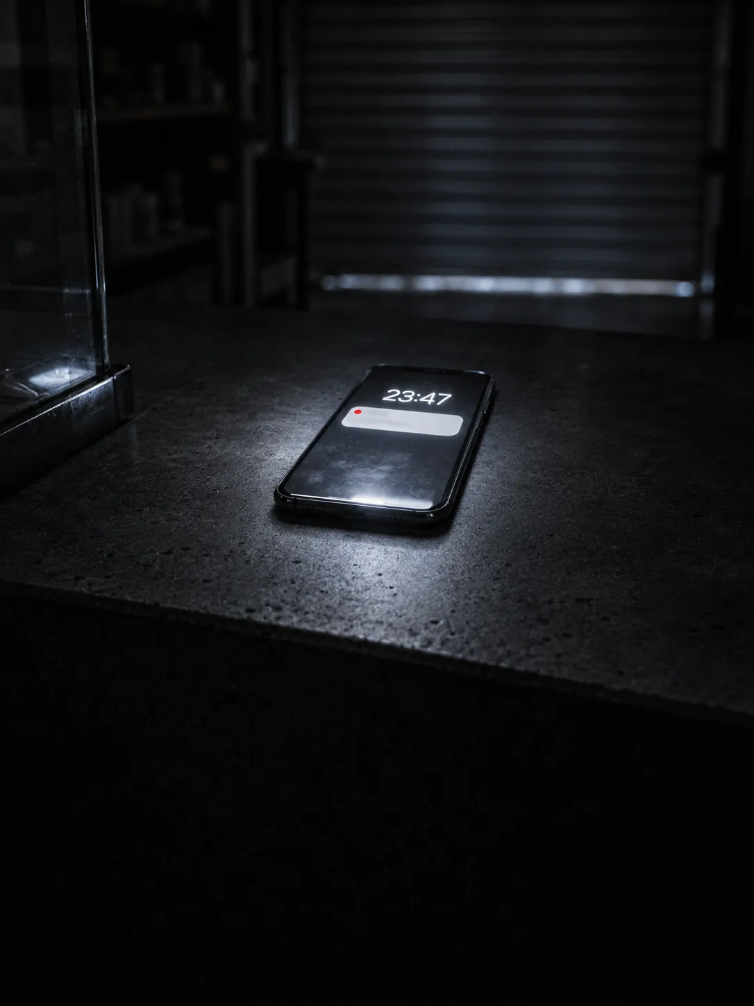 Celular sobre o balcão de uma loja fechada à noite, tela acesa às 23:47 com uma notificação sem resposta